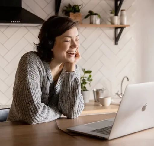 A woman smiles while working on her laptop, showcasing a positive and engaged expression