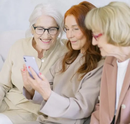 Three women examine a cell phone together, engaged in conversation and sharing a lighthearted moment